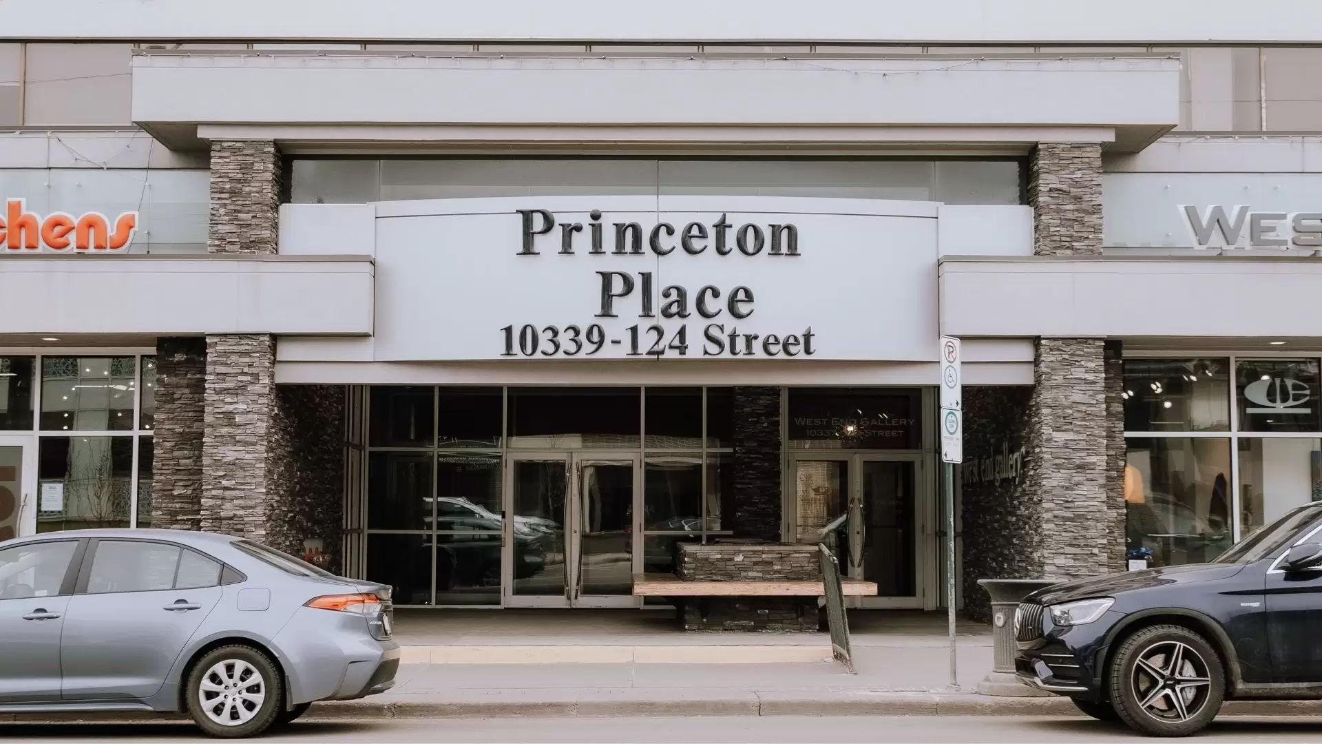 Front entrance of a grey office building with sign that says "Princeton Place 10339 - 124 Street" and two cars parked on the street.