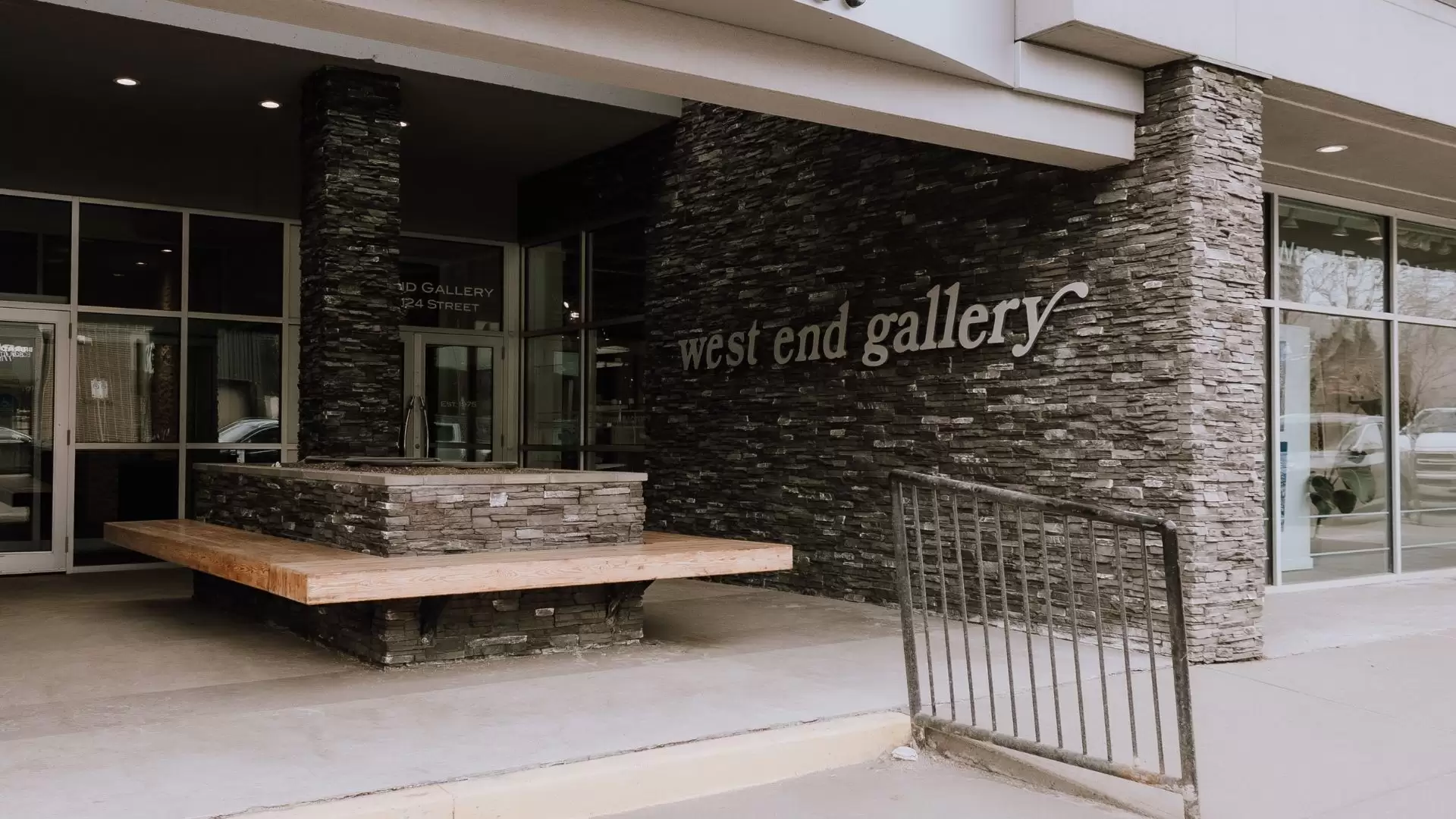 Princeton Place entrance with ramp and handrail. Wooden bench is in front of the glass doors and "West End Gallery" sign is on the brick wall.