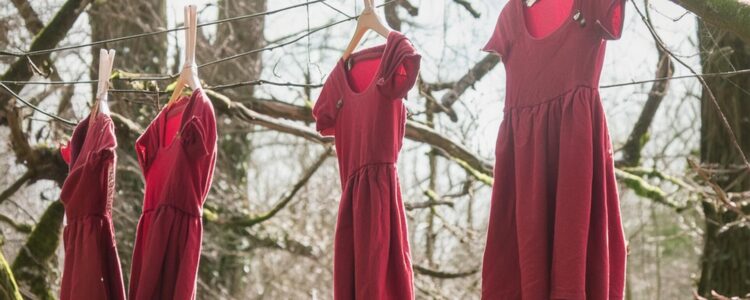 4 red dresses hanging from trees in the forest.